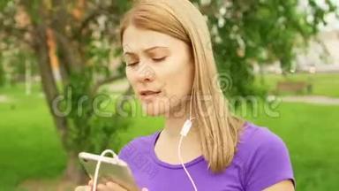 女人在公园里用耳机听手机音乐。 用她的智能手机跳舞唱歌